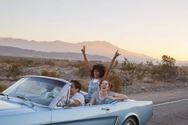 Group Of Friends On Road Trip Driving Classic Convertible Car