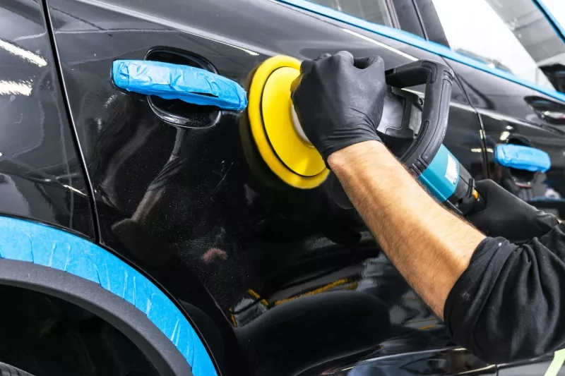 Car polish wax worker hands applying protective tape before polishing. Buffing and polishing car. Car detailing. Man holds a polisher in the hand and polishes the car