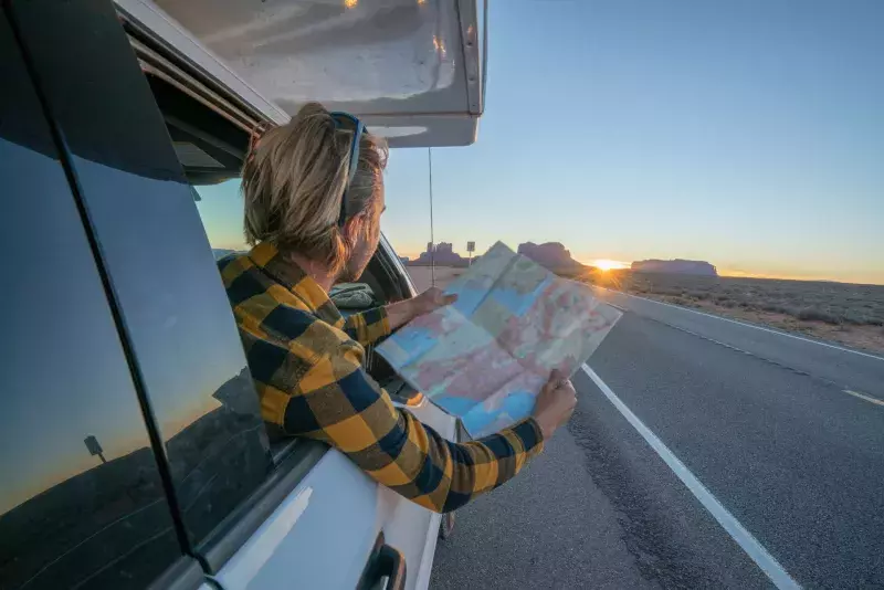 Road trip concept; Young man inside campervam looking at road map for directions exploring national parks and nature ready for adventure.