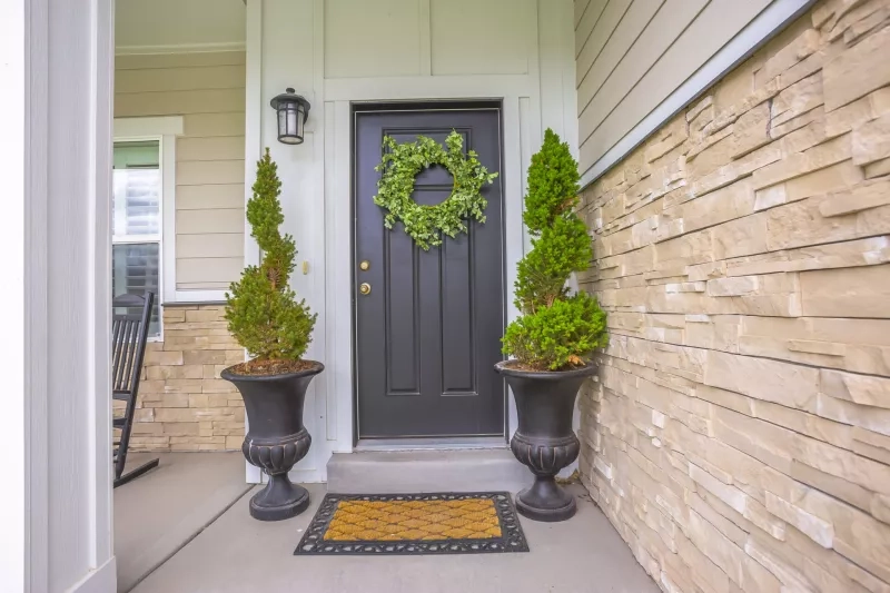 Gray front door of a home with green wreath and flanked by tall potted plants