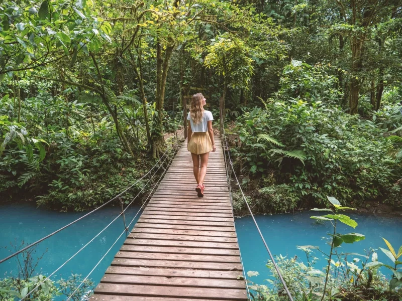 Young woman wandering in tropical rainforest walking on bridge over turquoise lagoon