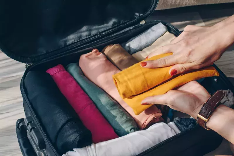 Top view of tourist woman open suitcase for pack and arranging colorful cloths for travelling.