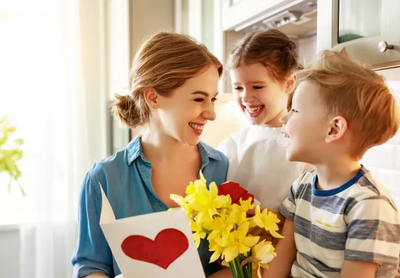 Happy children giving card and flowers to mother