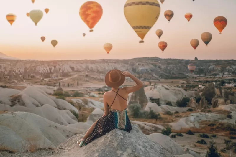 Back View Woman Sitting On The Ground Watching Balloons Looking At The Valley. Cappadocia sunrise