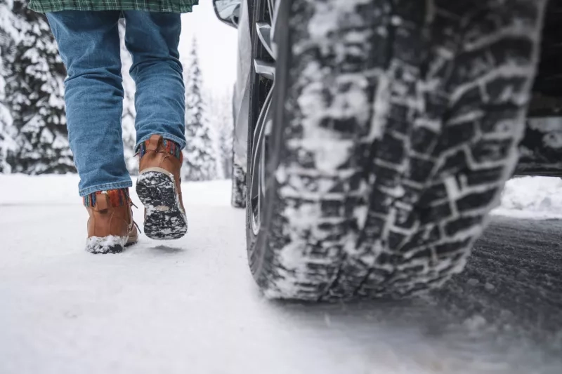 Low Section Of Woman Walking On Snowy Road Next To Vehicle