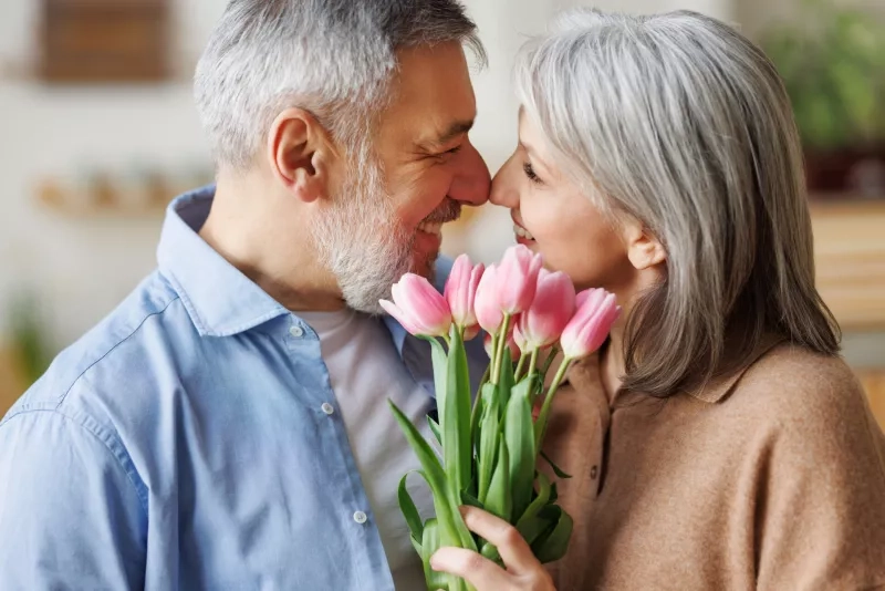 Loving senior husband giving wife bouquet of fresh pink tulips at home, congratulating on March 8