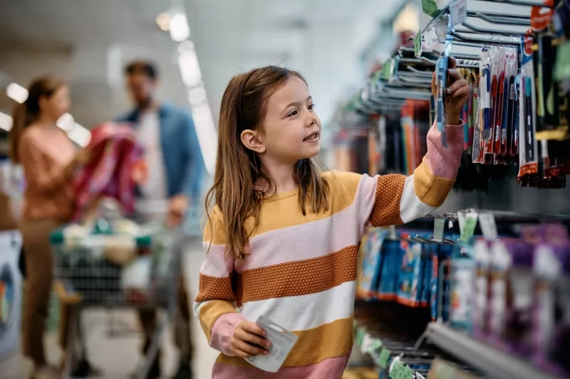 Smiling schoolgirl choosing products at school supplies section in supermarket.