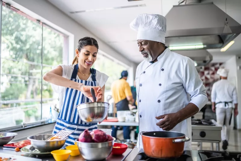 Student cooking and teacher helping in a cooking class