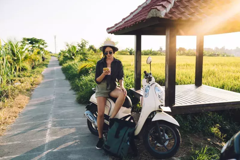 Millennial female user checking location information during online GPS tracking via modern cellphone gadget, travel girl resting on rent moped connecting to roaming internet for browsing website