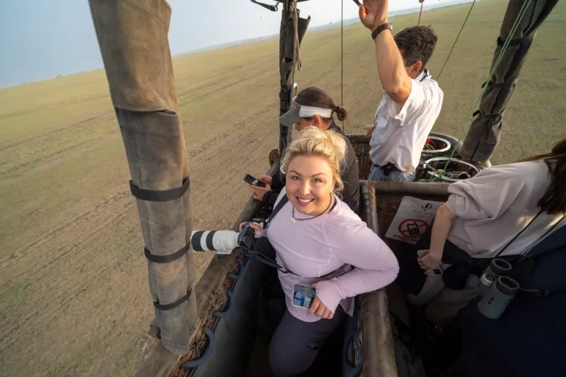 Happy tourists in a hot air balloon basket high over the Masaai Mara Reserve on an aerial safari