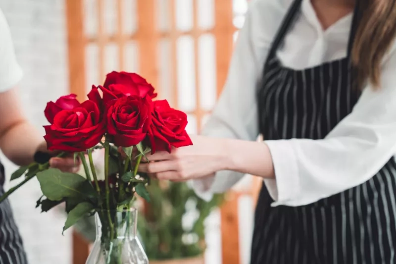 Several red roses are beautifully arranged in a glass vase ready to be delivered to customers order in a flower shop.