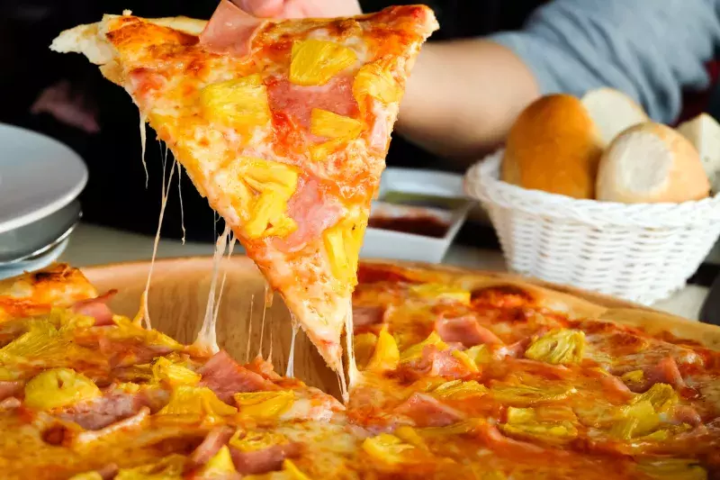 Close up Woman's hand picked Hawaiian pizza from a wooden tray on the table.